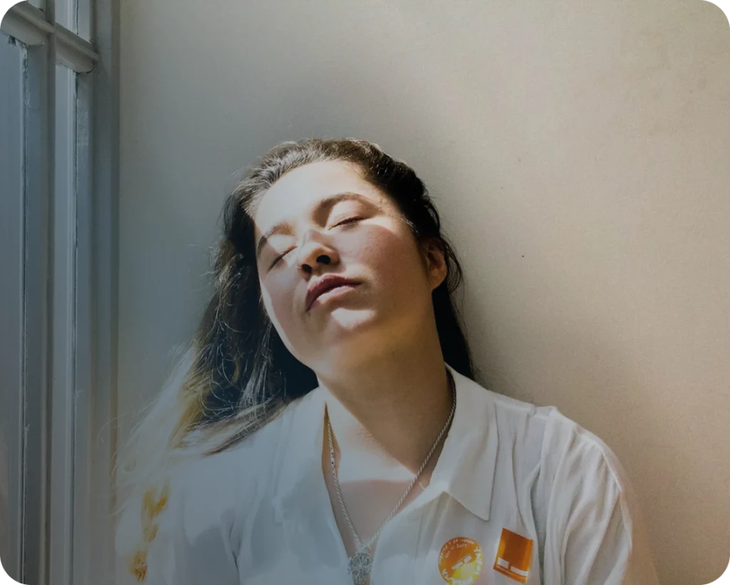 A sleepy woman next to a window.